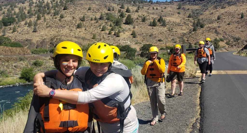 two students embrace in the foreground while others trail behind on a rafting expedition with outward bound